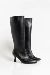 Botas altas de cuero negro con caña media, punta fina y taco aguja de altura media.