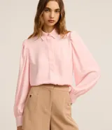 Camisa de crepé color negro, con cuello inglés, cierre frontal abotonado y mangas largas abullonadas con puños ajustados.