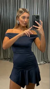 Vestido corto de lurex color azul marino con escote strapless, diseño ajustado con frunces laterales y falda con volado asimétrico.