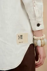 Chaqueta blanca de lino con cuello camisero, cierre con botones a tono, mangas largas con puños abotonados, bolsillos laterales y costuras a contraste.