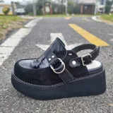 Zueco de cuero color marrón claro, con capellada en cuero negro con textura croco, tiras cruzadas frontales en cuero texturizado claro con hebilla metálica circular y tira ajustable en el talón. Cuenta con suela de plataforma corrida.