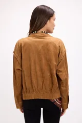 Campera de gamuza color beige con diseño de calados florales en hombros y espalda, cierre frontal y cuello camisero. Presenta un corte relajado y textura suave.
