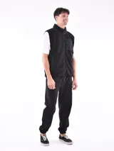 Chaleco de polar tipo corderito en color beige, con cuello alto y cierre frontal completo. Presenta un bolsillo de parche en el pecho en color azul marino con cierre de cremallera y ribetes en contraste en el mismo tono en sisas, cuello y bolsillos laterales.