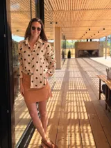 Camisa beige de muselina con estampado de lunares negros, cuello camisero, mangas largas con puños elásticos y cierre frontal con botones.