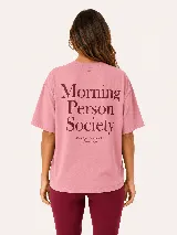 Remera oversize color rosado, con mangas cortas y estampado tipográfico en la espalda con la inscripción "Morning Person Society".