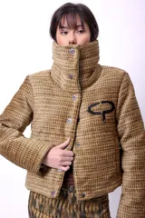 Campera corta con estampado abstracto en tonos marrones y beige, cuello alto, cierre frontal con botones a presión, bolsillos delanteros y bordado negro con las iniciales CP. Forro interior y relleno liviano de guata.