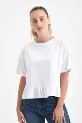 Remera blanca de manga corta y corte holgado, confeccionada en algodón orgánico, con detalle de volado fruncido en el ruedo.