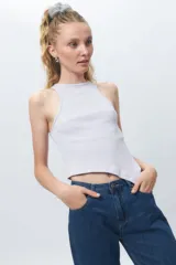 Top de algodón blanco sin mangas con cuello halter y bajo asimétrico en punta diagonal. Presenta un tejido de punto acanalado y un diseño inspirado en la estética de los años 2000.