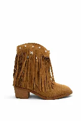 Bota corta de gamuza color camel, estilo cowboy, con flecos largos que cubren la caña y apliques metálicos plateados en forma de flor y un dije cuadrado con diseño tribal en el borde superior. Posee un taco bajo y ancho de madera.