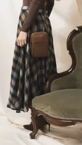 Bandolera pequeña de diseño compacto en color mostaza, confeccionada en material sintético con textura granulada. Presenta un bolsillo frontal con el logo de la marca impreso, cierre superior y correa ancha ajustable y desmontable.