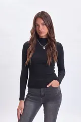 Remera de manga larga en color negro, confeccionada en tejido de punto acanalado con cuello alto ajustado.