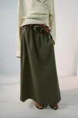 Falda midi tipo capa de tiro medio, confeccionada en mezcla de algodón color verde militar. Cuenta con cintura con trabillas, bolsillos de vivo en los laterales, cierre lateral con cremallera oculta y aplicación de cinturón marrón de estilo western con hebilla metálica grabada.