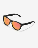 Lentes de sol Hawkers modelo One, con armazón negro mate y cristales polarizados con efecto espejado en tono rojizo.