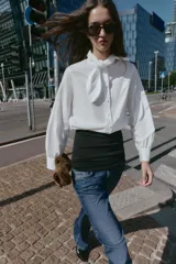 Camisa de popelín blanca con cuello solapa decorado con puntilla y lazo frontal. Presenta mangas largas con puños abotonados y cierre frontal con botones.