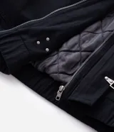 Campera de sarga de algodón con capucha, cierre frontal con cremallera y trabas metálicas decorativas. Presenta un bolsillo con cierre en la manga y puños elásticos, con un diseño de estilo utilitario.