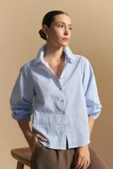 Camisa azul a rayas blancas, de manga larga con puños elastizados, entallada en la cintura y con cierre de botones frontales.