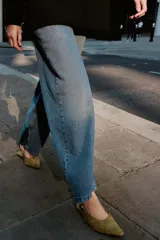 Zapato plano destalonado de punta fina, color verde oliva/mostaza, confeccionado en piel con acabado de gamuza. Posee una tira ajustable con hebilla metálica dorada en el talón.