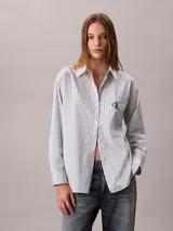 Camisa de Calvin Klein color celeste con patrón de rayas verticales finas y logo 'ck' bordado en el bolsillo frontal. Presenta cuello camisero, cierre frontal con botones y manga larga.