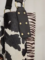 Cartera tipo hobo de cuero azul con textura granulada. Presenta un diseño holgado, con una correa de hombro bicolor que combina azul y rojo, sujeta por argollas metálicas. Incluye una placa metálica pequeña con el logo de la marca en la parte inferior frontal.