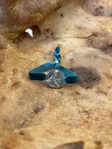 Pulsera plateada con dije circular con grabado y banda de terciopelo elástico color rojo.