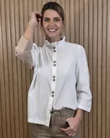 Camisa de algodón color blanco, con cuello alto con volados, mangas tres cuartos con detalles de bordado ingles y cierre frontal con botones de nácar.