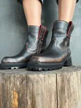 Bota de cuero con efecto desgastado en tonos marrones y negros, con suela track robusta y cierre lateral. Presenta detalles en color rojo en la parte superior de la caña.