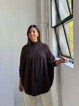 Poncho de punto color chocolate con cuello alto y diseño de trenzas verticales en el frente. Presenta mangas tres cuartos con puños acanalados y un corte holgado y fluido.