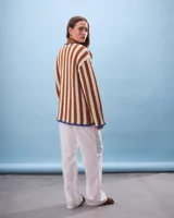 Cárdigan tejido a rayas verticales color marrón y beige, con cuello marrón, cierre con nudos azules y bolsillos frontales ribeteados en azul.
