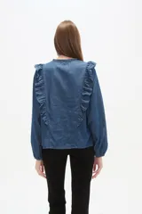 Blusa de jean con volados frontales, cuello redondo con abertura en V y lazo para anudar, y mangas largas con puños elásticos.