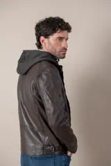 Campera de cuero negro con capucha gris desmontable, cierre frontal, bolsillos con cierre y detalles de hebillas en el cuello y la cintura.