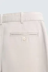 Pantalón de corte relajado confeccionado en tejido de algodón con estructura twill. Presenta pliegues frontales, bolsillos laterales y bolsillos traseros de doble vivo con botón. Cierre frontal con cremallera y botón.