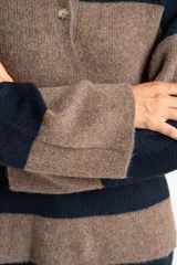 Sweater de tejido de punto color blanco roto o crema, con textura jaspeada. Presenta cuello polo y un escote con tres botones nacarados. El calce es holgado (oversize) y tiene mangas largas.