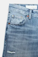 Jeans de tiro bajo y cinco bolsillos, con diseño de pierna ancha y larga. Presenta roturas y desgastes sutiles en la parte delantera. Cierre frontal con cremallera y botón metálico.