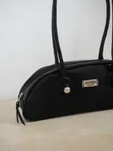 Cartera estilo baguette de cuero con silueta alargada y compacta, diseñada para llevar bajo el brazo. Presenta manijas largas con detalles de nudos esféricos metálicos en las uniones.