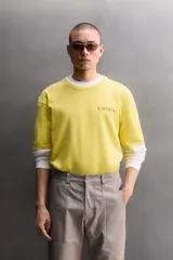 Camiseta de corte relaxed fit color amarillo, confeccionada en tejido compacto de algodón, con cuello redondo, manga corta y estampado frontal a contraste con texto y motivo floral pequeño.