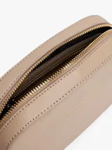 Cartera tipo camera bag de Tommy Hilfiger en color beige, con acabado granulado y logo de la marca en letras doradas en el frente. Cuenta con cierre de cremallera superior, compartimento principal, bolsillo interior abierto y bolsillo interior con cremallera. Incluye una correa ajustable de tejido textil con detalles distintivos de la marca.