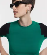 Blusa de viscosa con cuello redondo y mangas cortas. Presenta un diseño de bloques de color contrastantes, con cuerpo en tono malva y mangas en color negro, destacando por sus recortes asimétricos en la sisa.