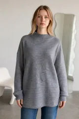 Sweater de punto color crema, con cuello alto y diseño holgado. Presenta puños y ruedo acanalados con detalle de líneas horizontales en la parte inferior.