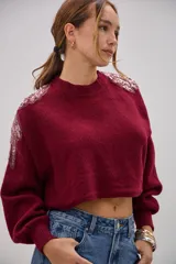Sweater de punto color bordó, de corte cropped y mangas largas con puños ajustados. Presenta detalles decorativos de apliques bordados con lentejuelas y perlas en la zona de los hombros.