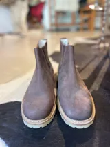 Botas chelsea de caña baja en color marrón, confeccionadas en cuero con elásticos laterales y suela dentada de goma.