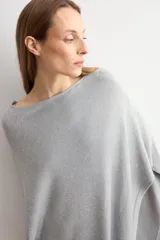 Capa tejida en hilo de lurex color beige, con cuello bote y diseño asimétrico de corte fluido.