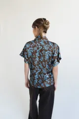 Blusa de seda con estampado floral en tonos marrón y celeste, con cuello alto, manga corta japonesa y cierre cruzado con botones negros visibles en diagonal.