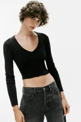 Top de punto ajustado de color negro, de manga larga y escote en V. Cuenta con la espalda descubierta con tirantes finos cruzados y cordón ajustable en el bajo.