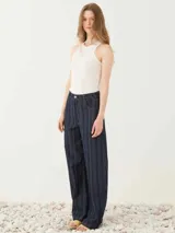 Pantalón de cinco bolsillos de tiro alto y pierna amplia con diseño de rayas finas verticales, confeccionado en tejido denim con cierre frontal de botón y presillas para cinturón.