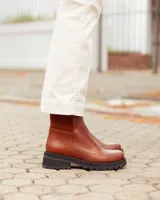 Botas cortas de cuero color marrón con suela track negra de goma. Presentan un diseño de corte clásico con paneles laterales texturizados y cierre lateral interno.