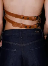 Top de cuero color camel, de diseño estructurado con tirantes ajustables mediante hebillas metálicas y cierre frontal con hebilla.