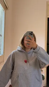 Canguro gris de algodón con felpa, de corte holgado y diseño clásico con capucha y bolsillo frontal tipo canguro. Presenta un bordado en el pecho y un aplique decorativo de piedras en forma de corazón.