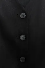 Chaleco negro con cuello en pico, sin mangas, bolsillos delanteros de vivo y cierre frontal con botones a contraste.