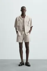 Bermuda de corte relajado color beige claro, confeccionada en lino. Presenta cintura elástica con cordón ajustable y bolsillos laterales y traseros.