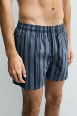 Bañador de hombre de largo medio, color azul claro con rayas verticales en azul oscuro. Posee cintura elástica ajustable con cordón, bolsillos laterales y un bolsillo trasero de plastrón.